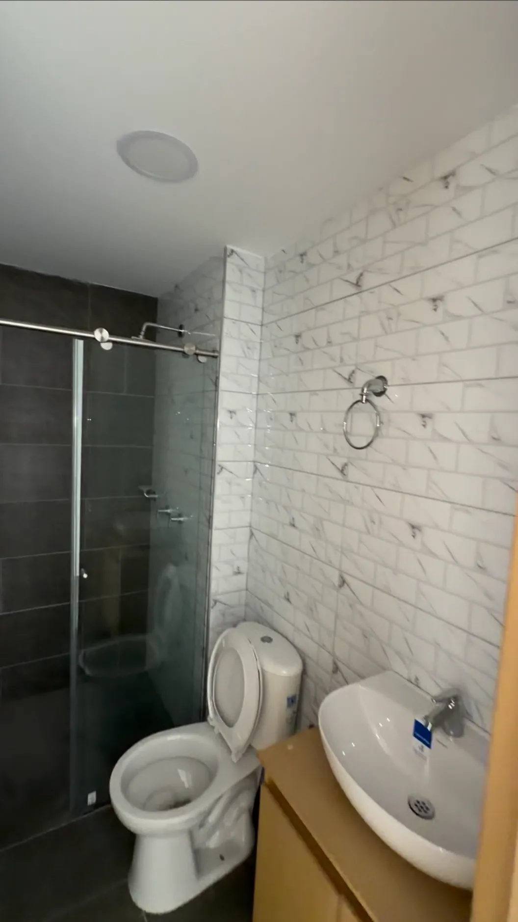 Baño con ducha de vidrio, enchape de ladrillo blanco y lavamanos