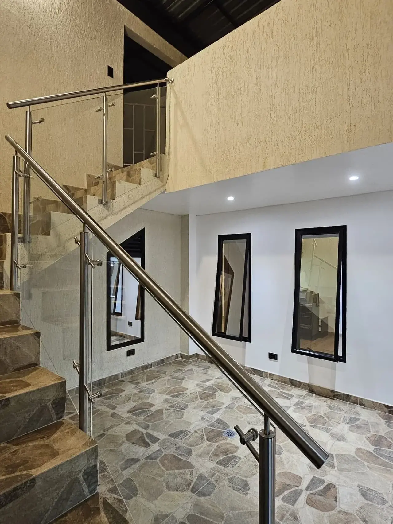 Escalera con baranda de vidrio y acero, piso de piedra y ventanas