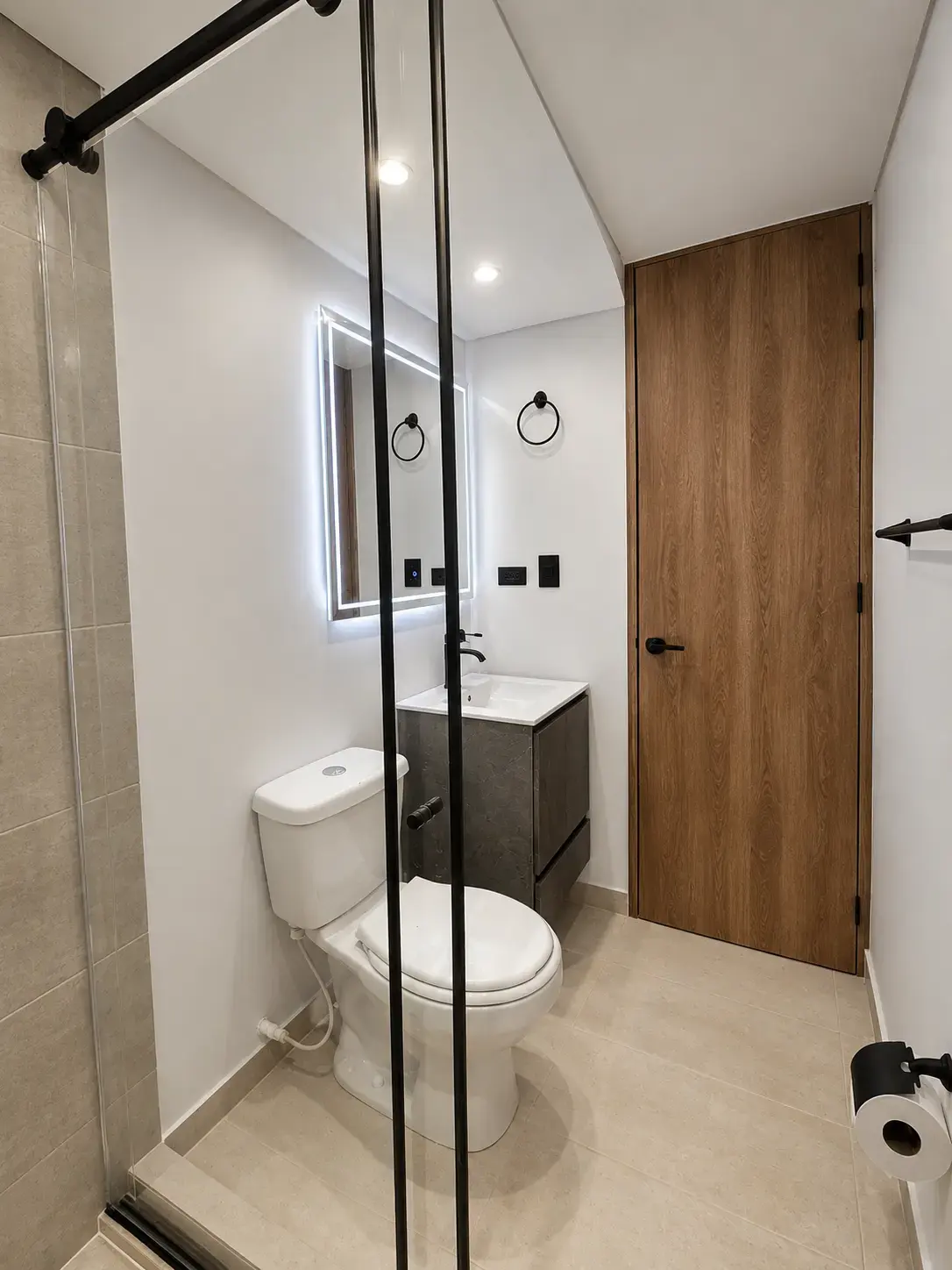 Baño con ducha de vidrio, espejo con luz LED y puerta de madera