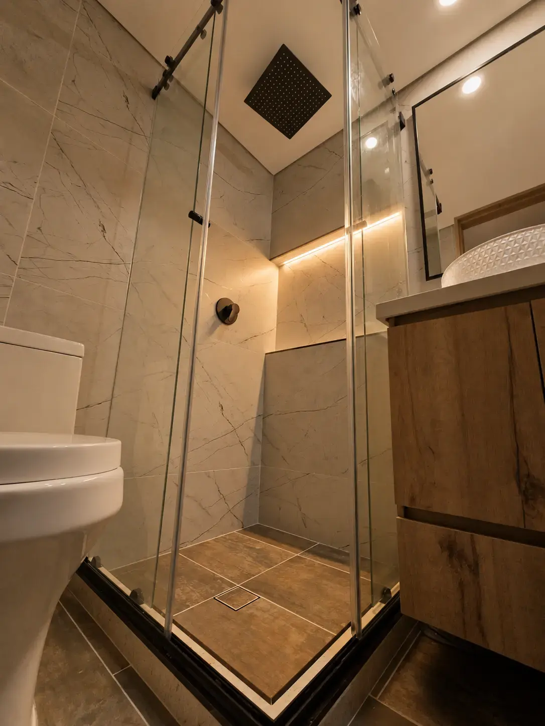 Baño con ducha de vidrio, sanitario y mueble de madera, vista lateral