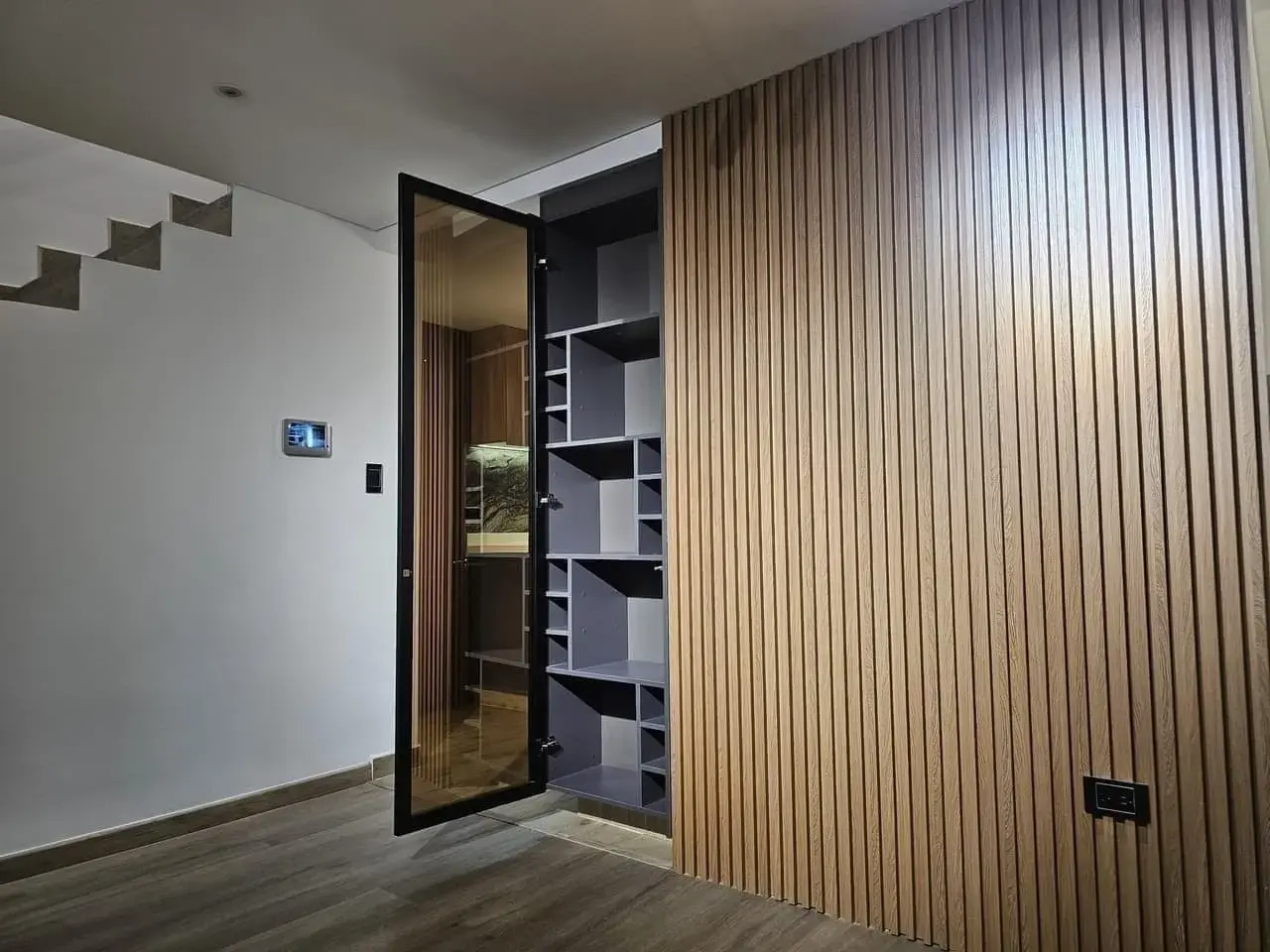 Muro de listones de madera y puerta de vidrio con repisas junto a la escalera