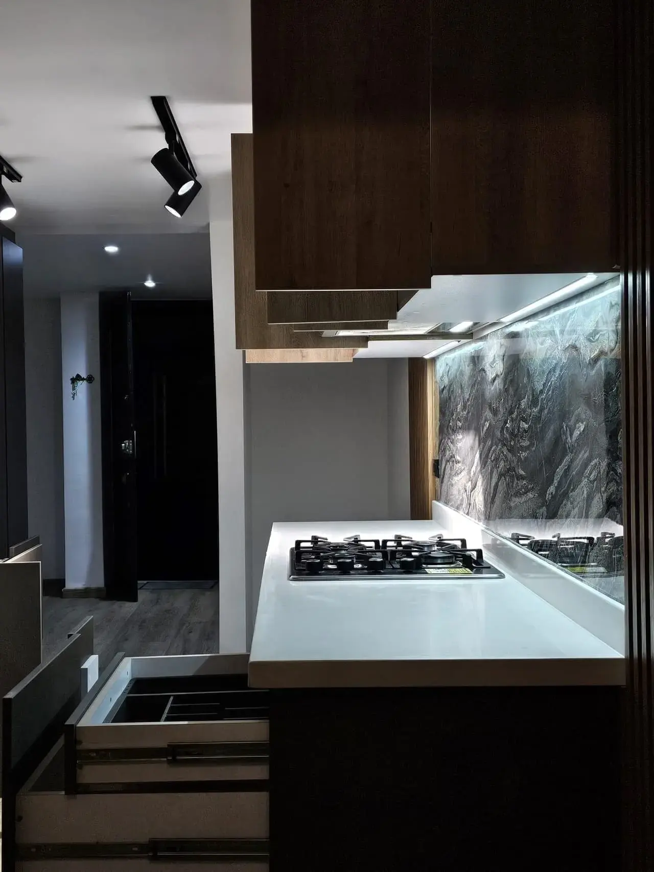 Cocina con estufa de gas, mesón blanco, gabinetes con cajones y luz LED