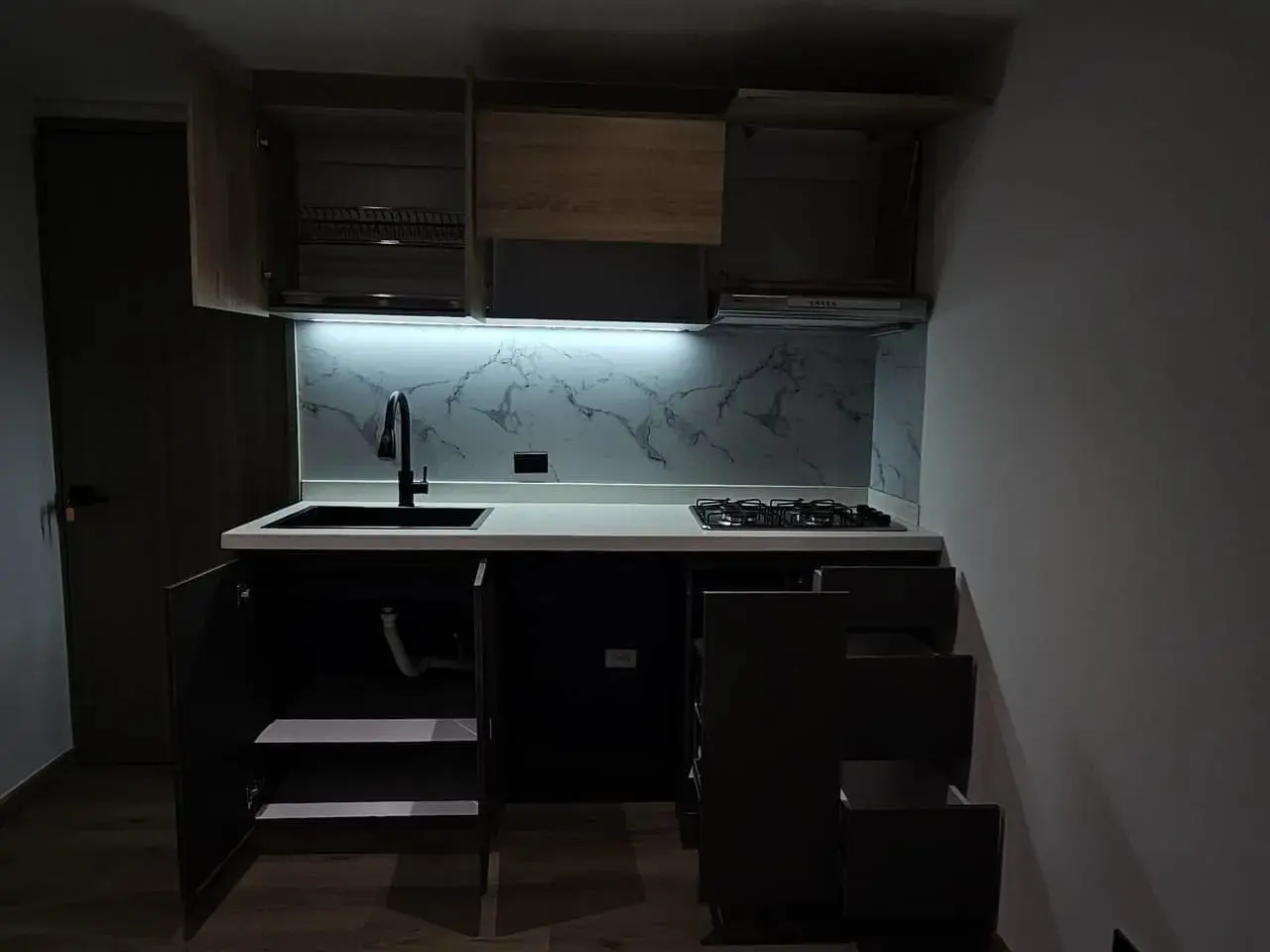 Cocina compacta oscura con gabinetes, lavaplatos y luz LED