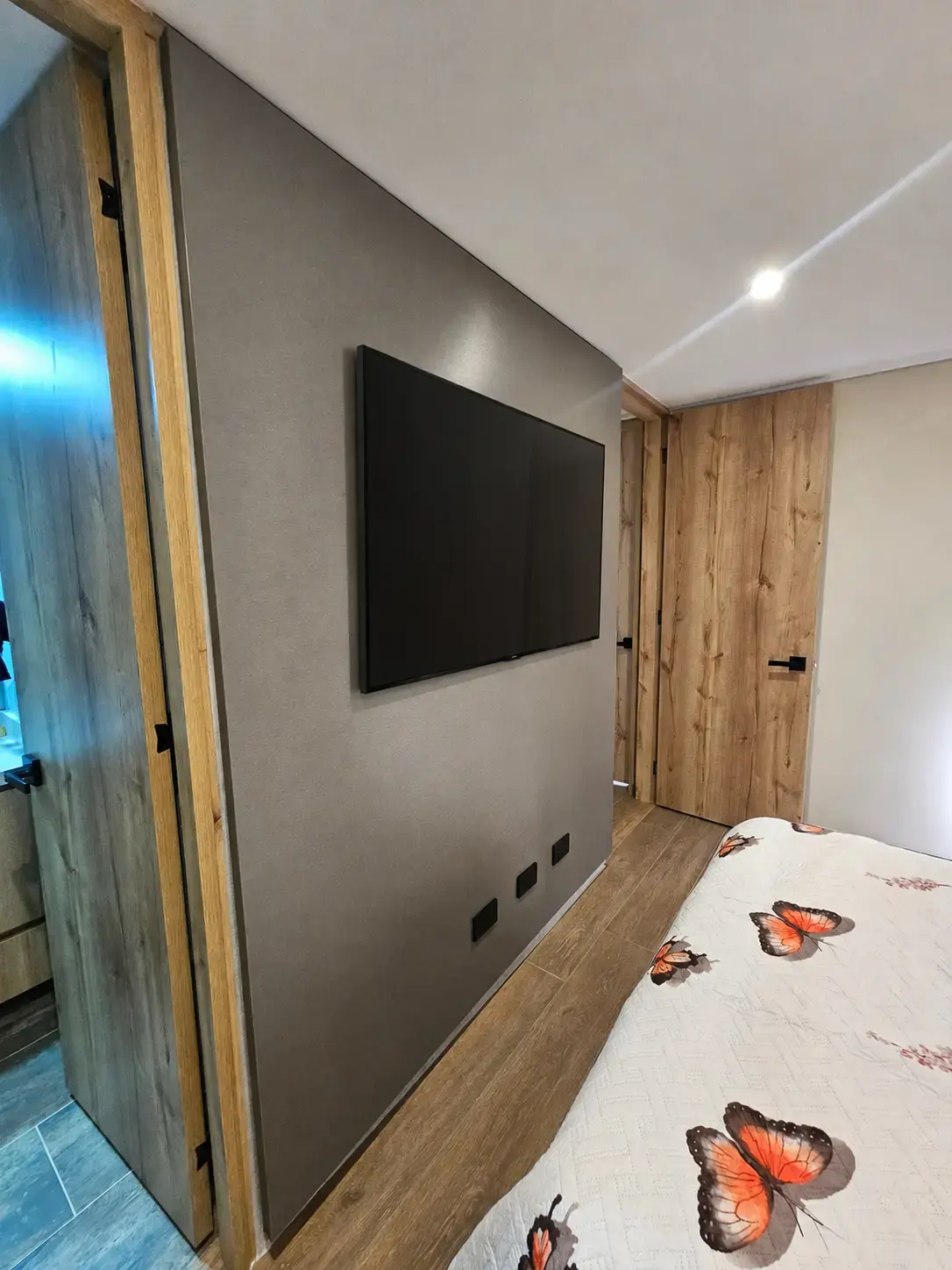 Habitación con televisor sobre pared gris y puerta de madera