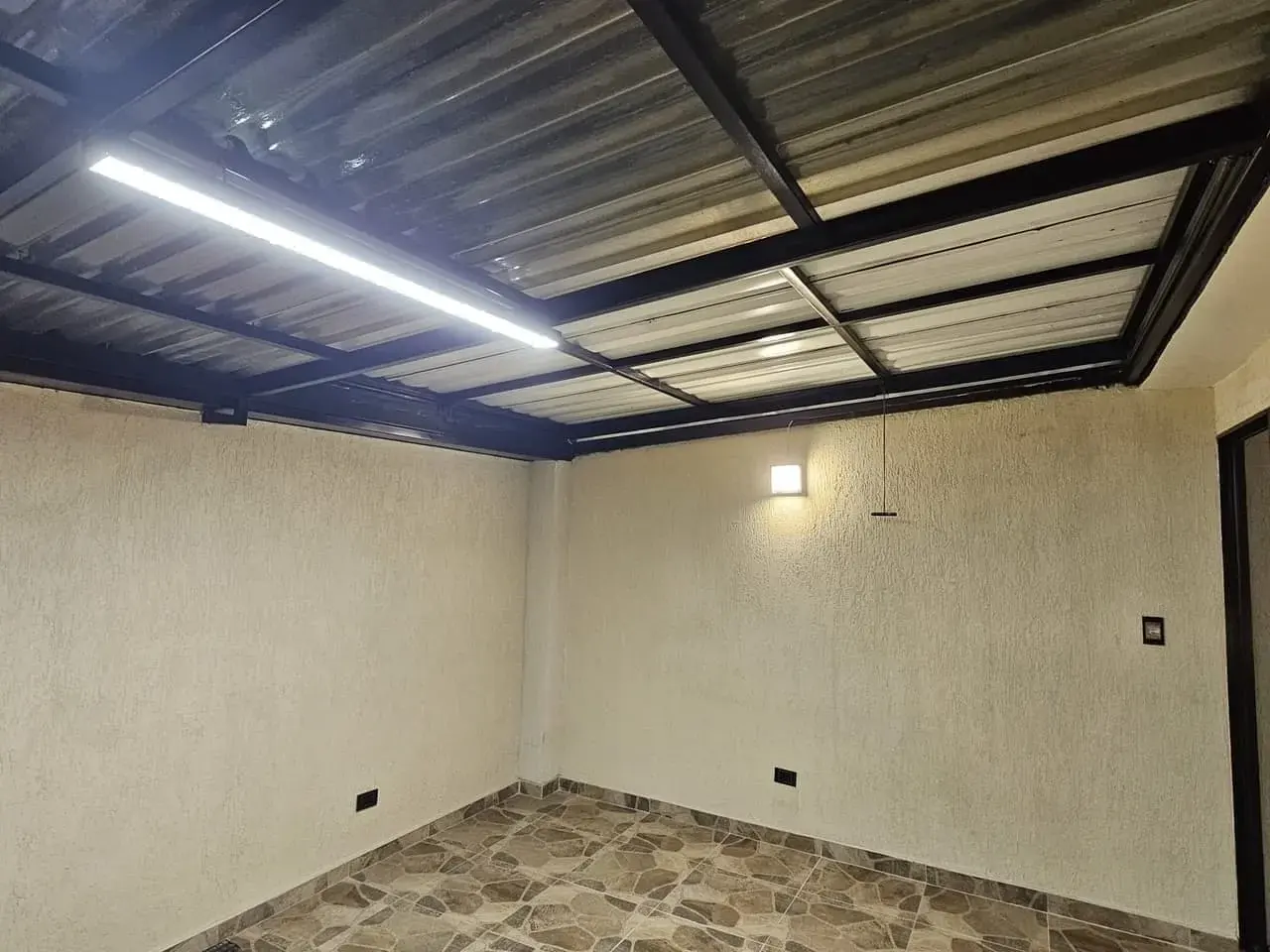 Espacio cubierto con techo metálico, luz lineal y piso de piedra