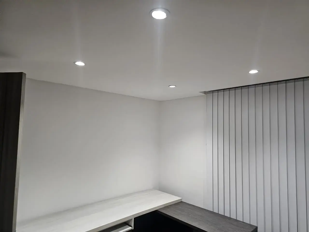Esquina de estudio con escritorio blanco y cortinas verticales