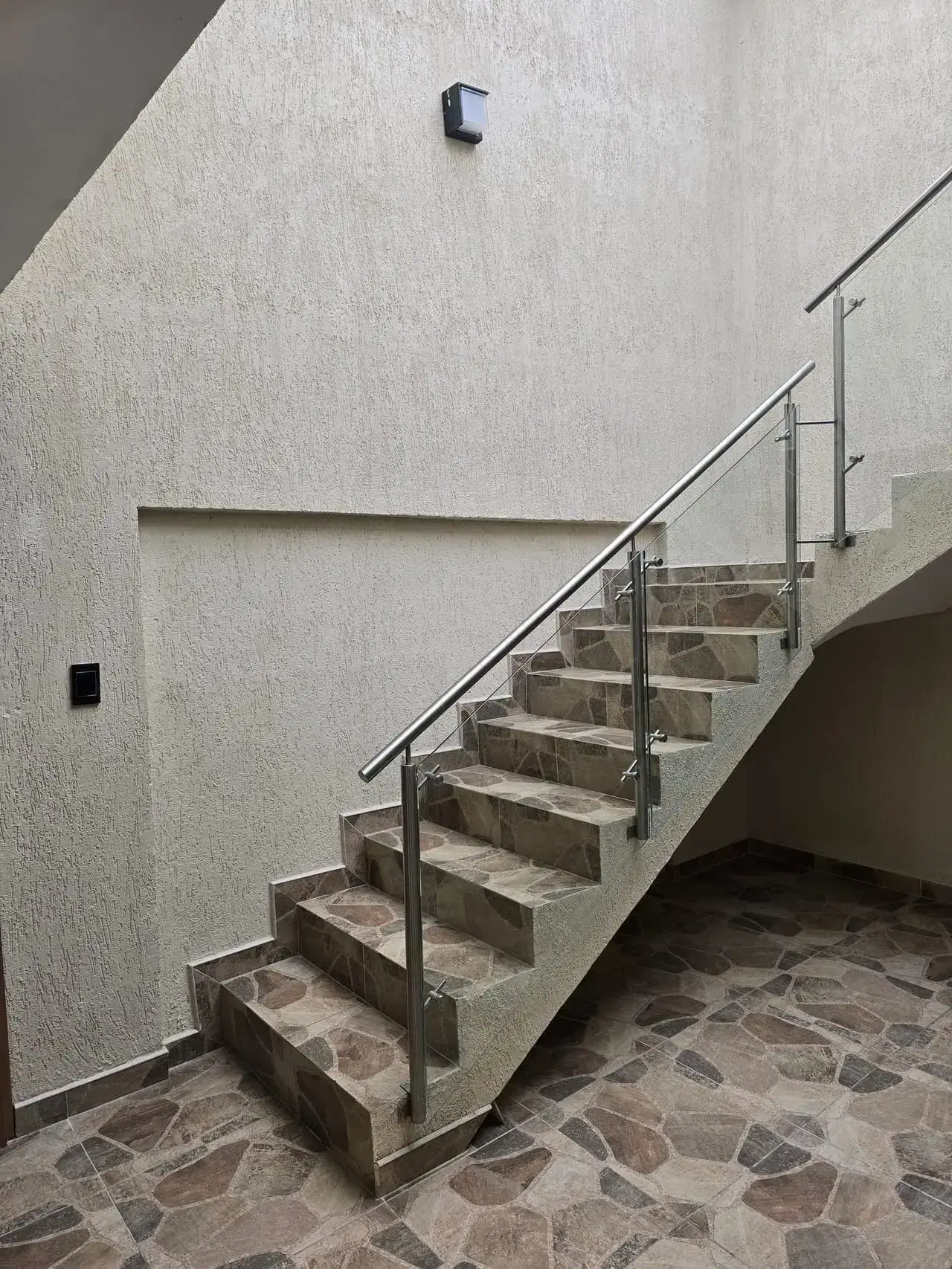 Escalera con baranda de vidrio y acero sobre piso de piedra