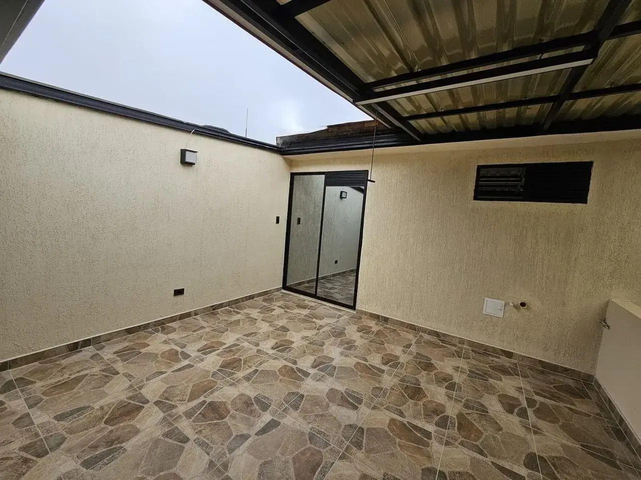 Patio cubierto con puerta de vidrio y piso de piedra