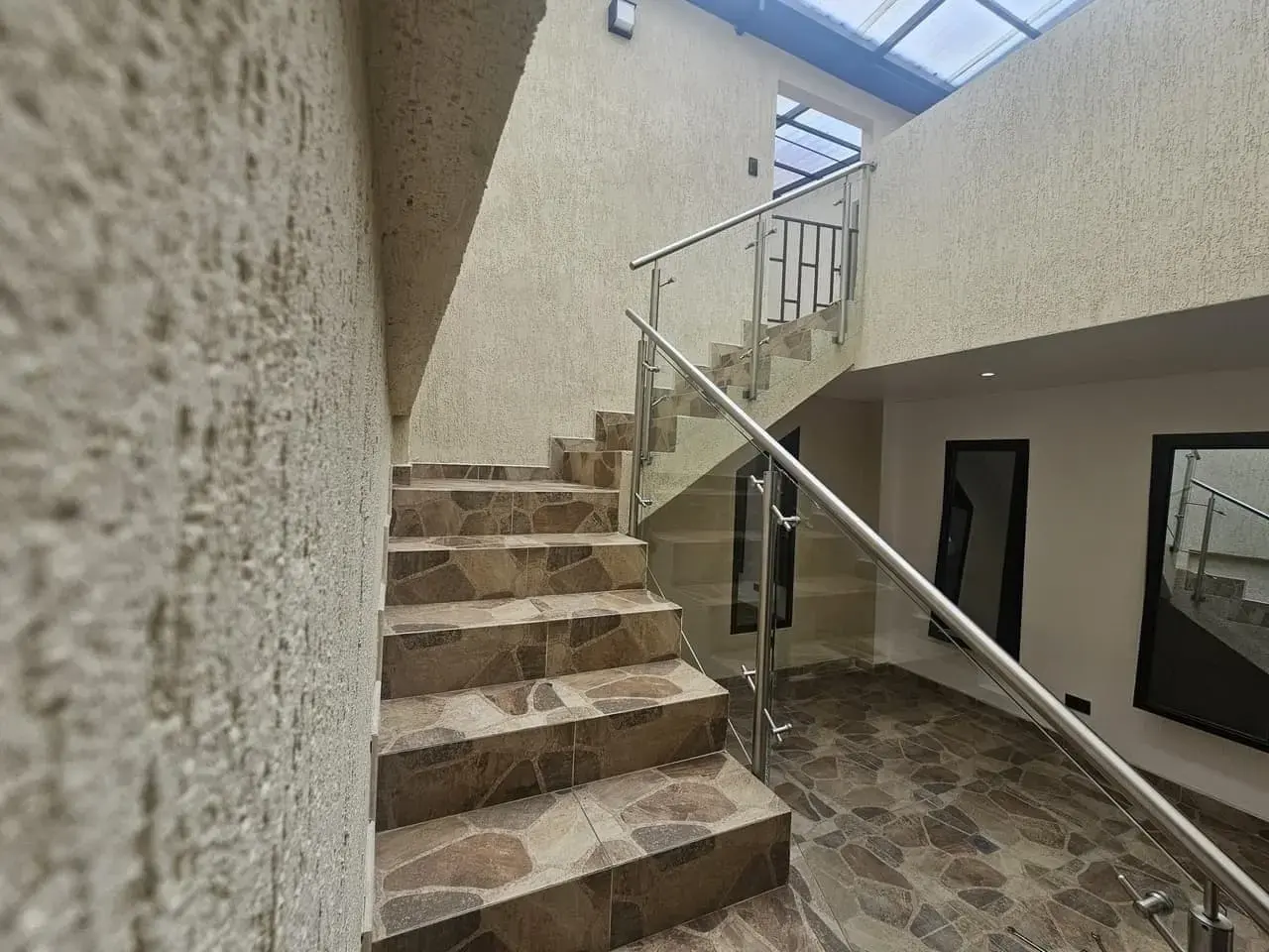 Escalera con baranda de acero y vidrio bajo una claraboya