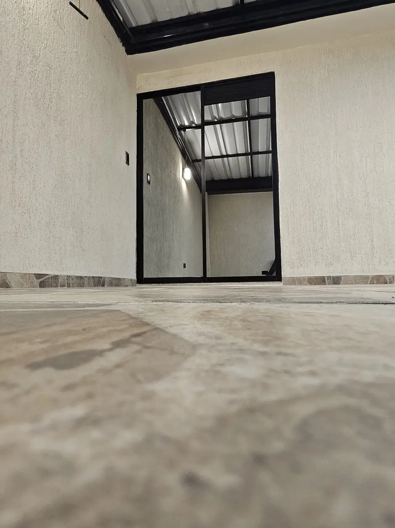 Espacio con ventana de vidrio y marco negro, piso de piedra y techo metálico
