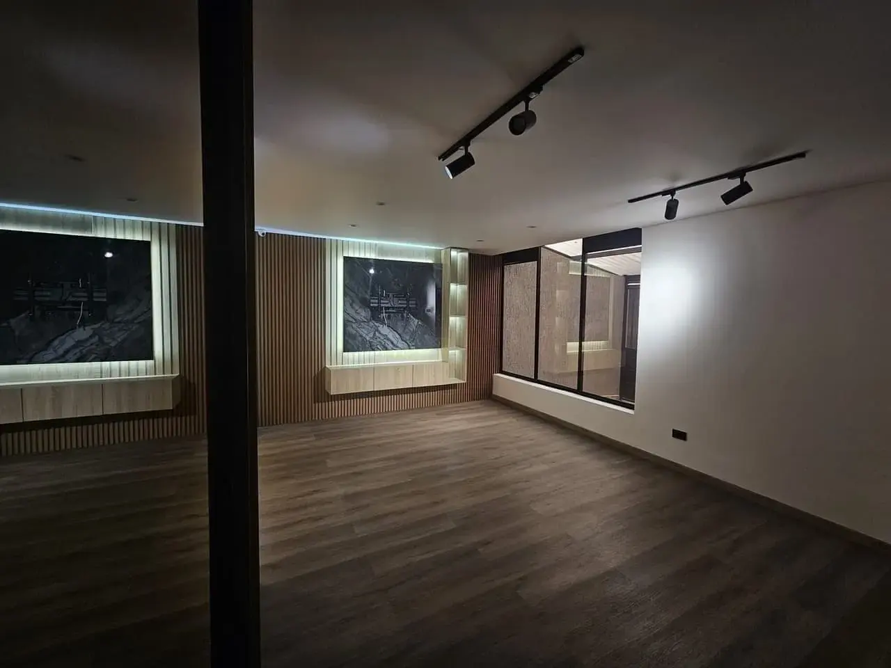 Sala con pared de listones de madera, columna y riel de luces